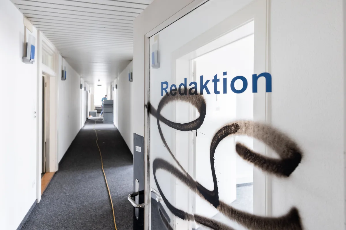 Man sieht den Eingang in ein Büro. Auf einer Glastüre steht Redaktion geschrieben. Die Türe ist mit schwarzer Farbe besprayt.